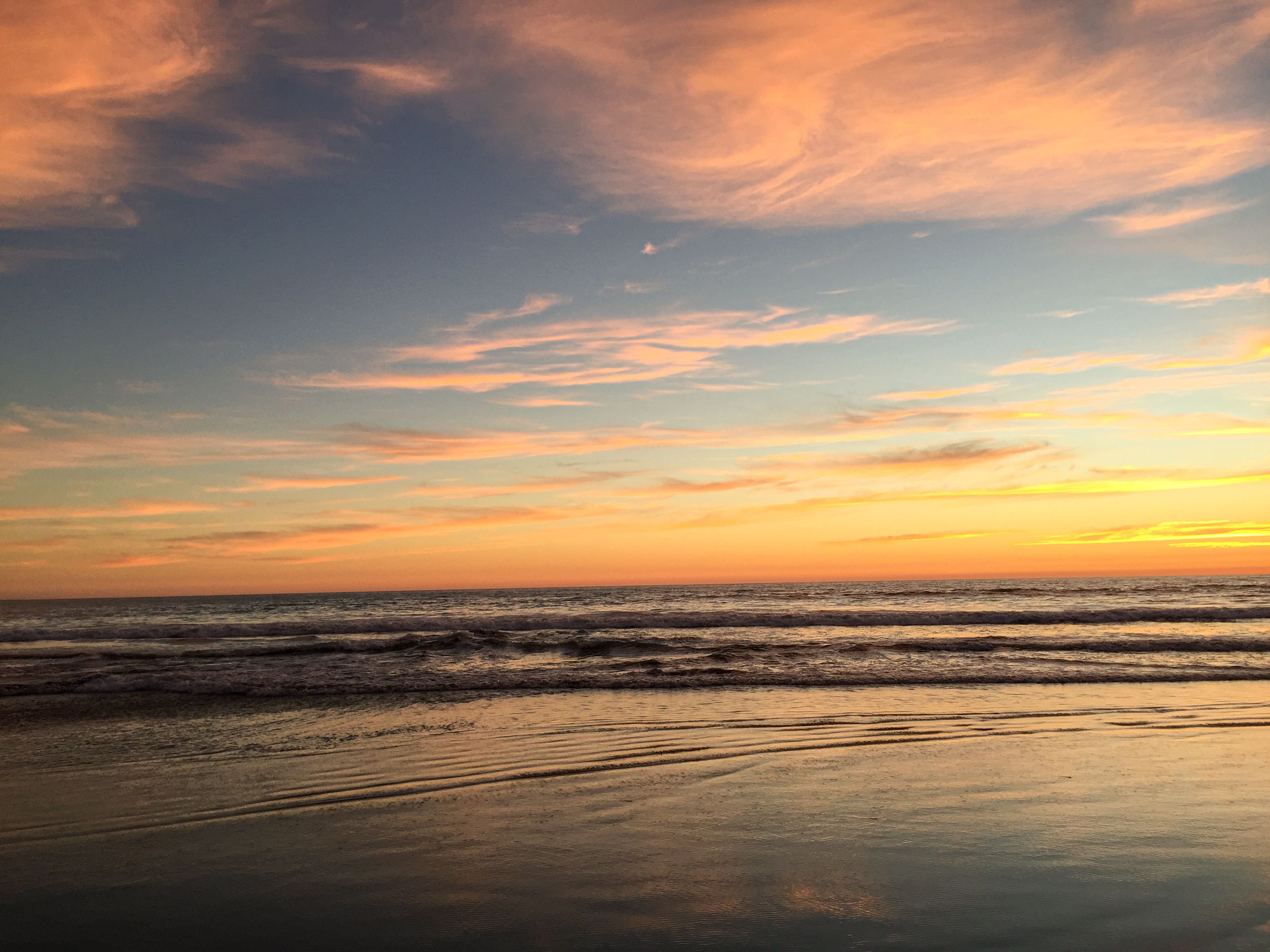 A wide ocean shore scene at sunset with magenta clouds, deep blue sky, and metallic water.